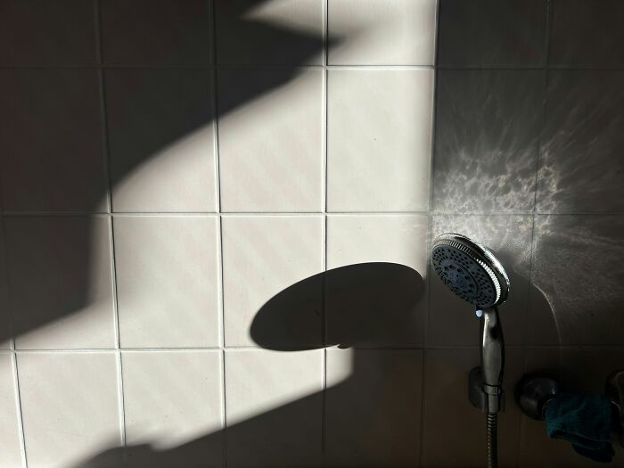 Shower head casting a shadow on bright bathroom tiles.