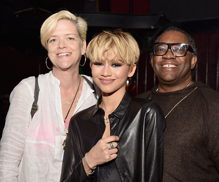 Zendaya smiling with two people, wearing a black leather jacket, amid family rift news.