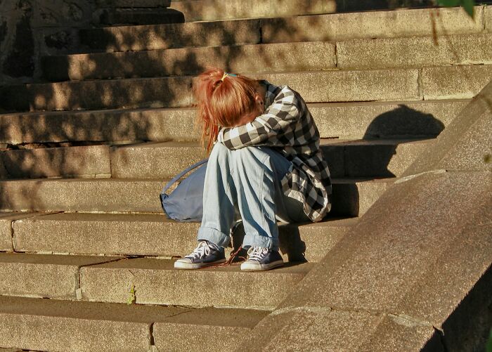 Person sitting on steps, head down in arms, seemingly reflecting on an insignificant thing stuck forever.