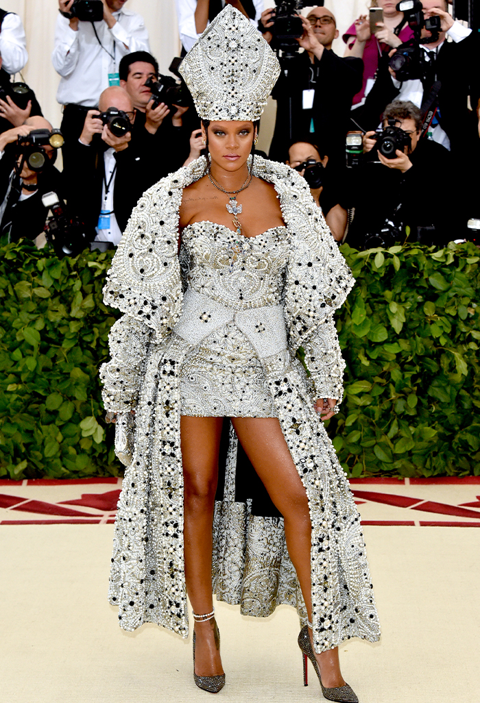 Celebrity in elaborate silver ensemble and high heels on red carpet amidst photographers.