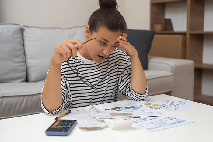 Woman reviewing late father’s estate documents looking stressed and overwhelmed while sitting in a living room. Woman reviewing late father’s estate documents looking stressed and overwhelmed while sitting in a living room.