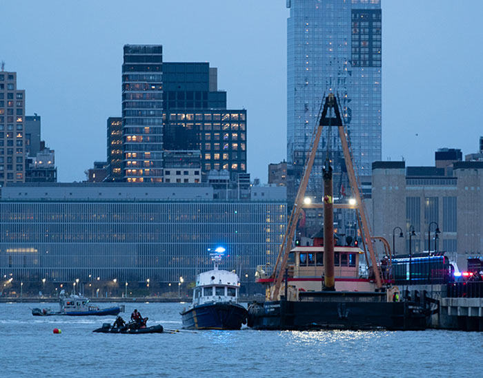 Rescue boats near NYC harbor after helicopter crash, with city skyline in background.