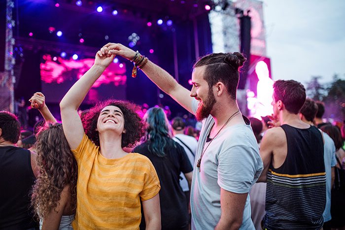 Couple dancing joyfully at a music festival, surrounded by a lively crowd under colorful lights. Couple dancing joyfully at a music festival, surrounded by a lively crowd under colorful lights.