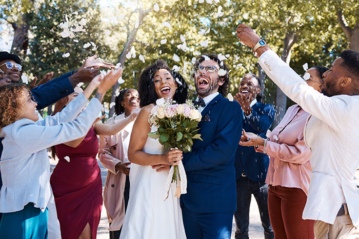 Bride and groom celebrate with guests throwing petals, outdoors after wedding ceremony.