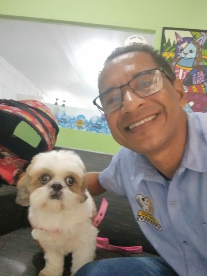 Man taking a selfie with a dog in his pet taxi service, both looking at the camera in a colorful room.