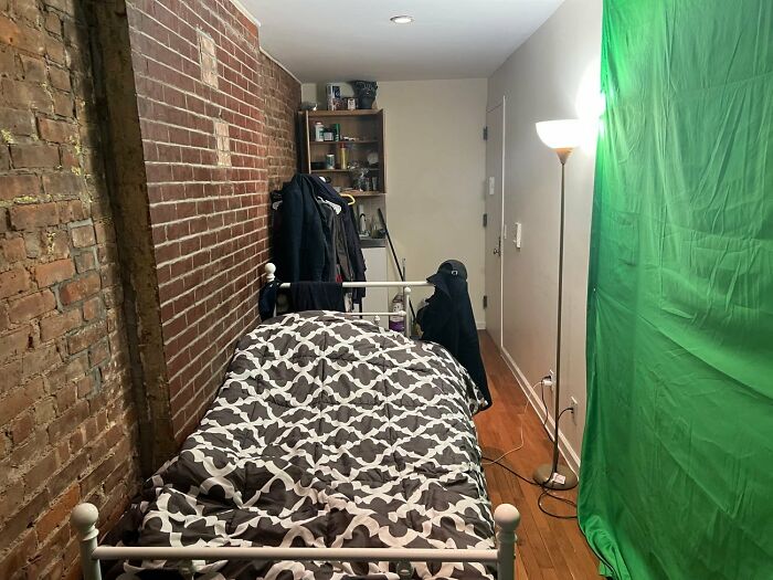 Small bedroom with exposed brick wall, patterned bedspread, and a green screen setup illustrating things that look awesome in movies.