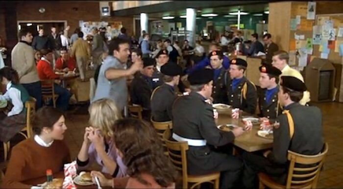 Group of uniformed men and civilians eating in a crowded cafeteria, illustrating things that look awesome in movies but are terrible in real life.
