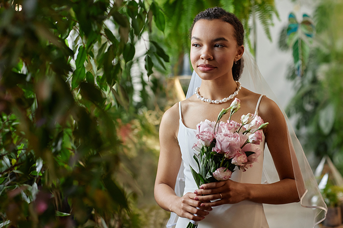 Bride holding a bouquet, standing amidst greenery at her wedding.