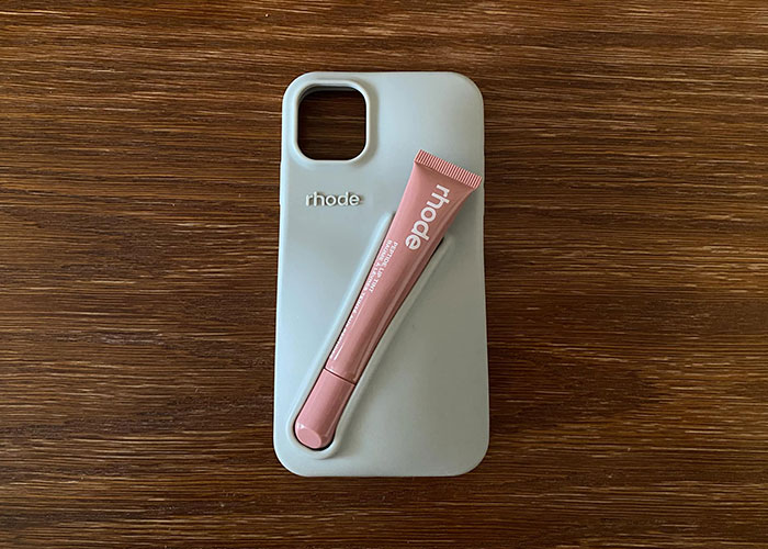 Expensive phone case with a pink lip product on a wooden surface.