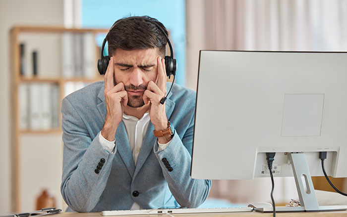Frustrated man with headset at computer, facing client escalation issue at work.
