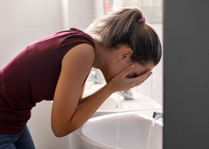Woman in distress leaning over a sink, possibly reflecting family chaos from exposed affair during rehearsal dinner.