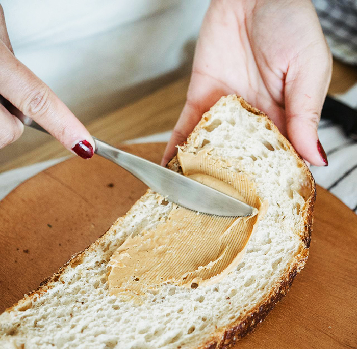Grandma spreading peanut butter on bread with a knife, highlighting nuts in a family food context.