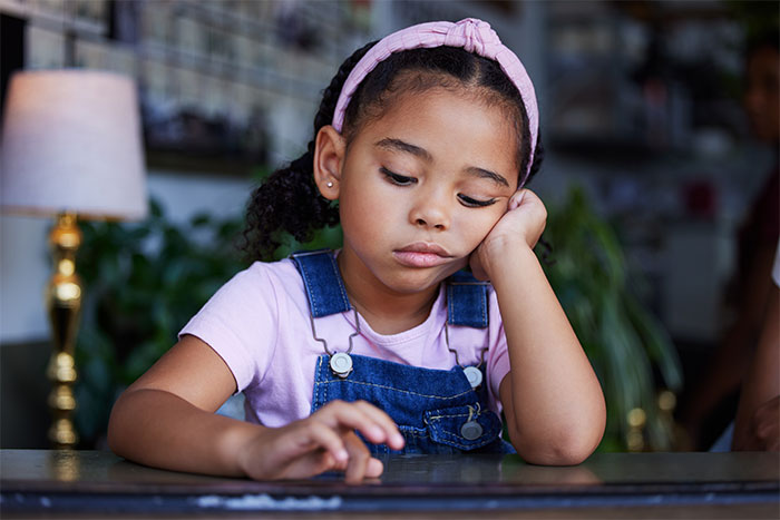 Young girl looking sad, wearing a pink headband and denim overalls, related to a babysitting incident about "unruly" hair.