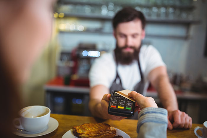 Customer paying at a cafe counter, employee in apron handling card reader. Customer paying at a cafe counter, employee in apron handling card reader.
