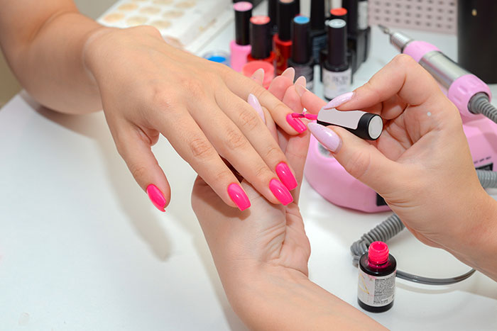 Woman getting bright pink nails painted at a nail salon, showcasing vibrant color options available.