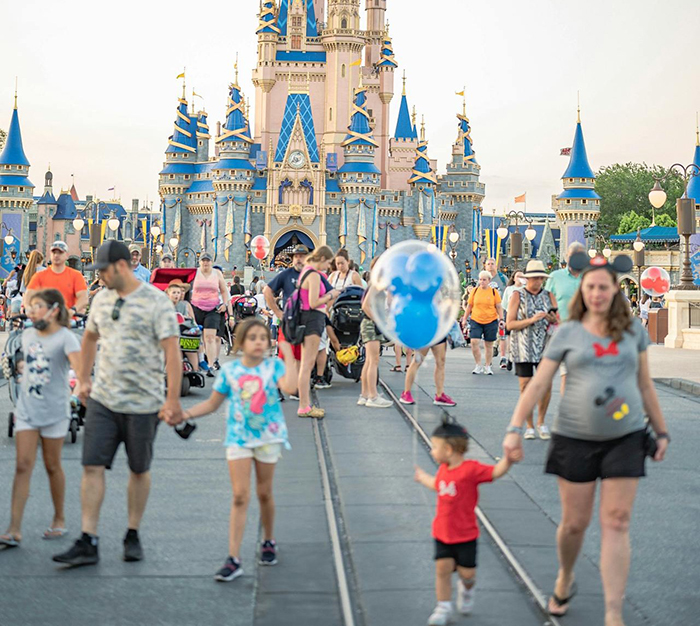 People walking near a castle in a busy theme park, enjoying a vacation spot.