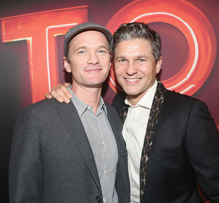 Two smiling men pose together at an event, wearing suits.