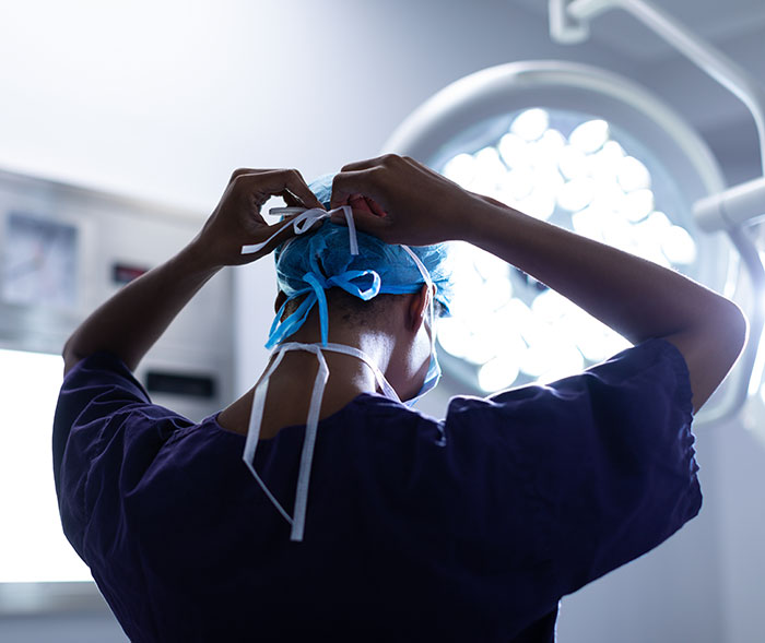 Person in surgical scrubs, back view, adjusting cap under operating room light, symbolizing plastic surgery.