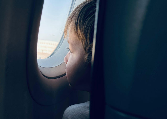 Child looking out of airplane window, capturing a travel moment mid-flight.