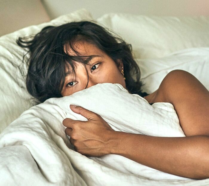 Woman in bed, looking pensive, highlighting issue of pain meds prescription inequality.