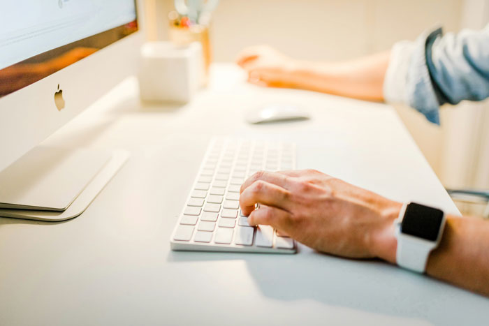 Person wearing smartwatch typing on a keyboard at a desk, focusing on submitting SEO deliverables efficiently.