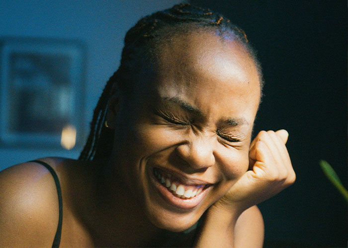 Smiling woman with braided hair in warm lighting, expressing joy and relaxation, symbolizing marriage cheat code insights.