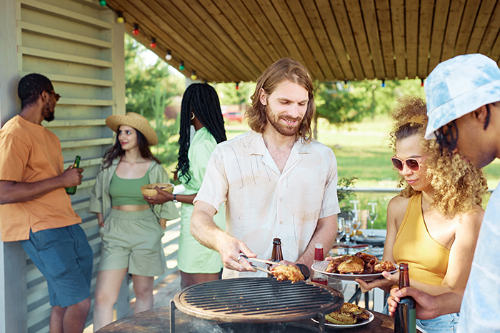 Man cooking gluten-free meal at a barbecue, surrounded by friends, outdoors under a wooden pergola.