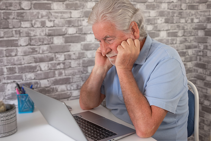 Elderly father looking at laptop, worried about vacation house security cameras.