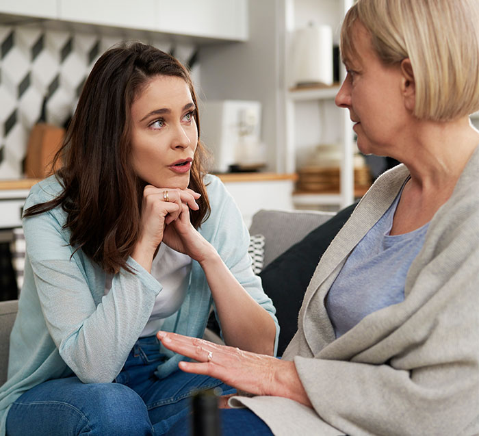 Two women engaged in a discussion about modern grandparenting double standards in a cozy living room.