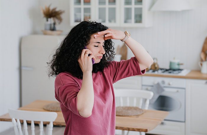 Woman on phone appearing stressed in a kitchen, related to neighbors in her late mom's house.