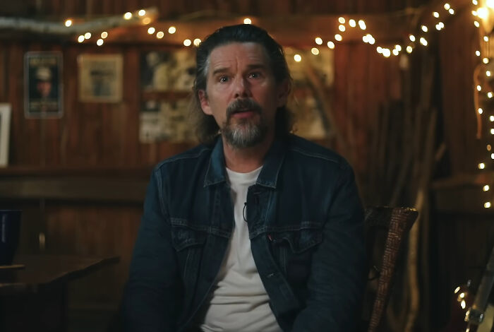 A celebrity in a dimly lit room, wearing a denim jacket, admired for being one of the nicest by netizens.