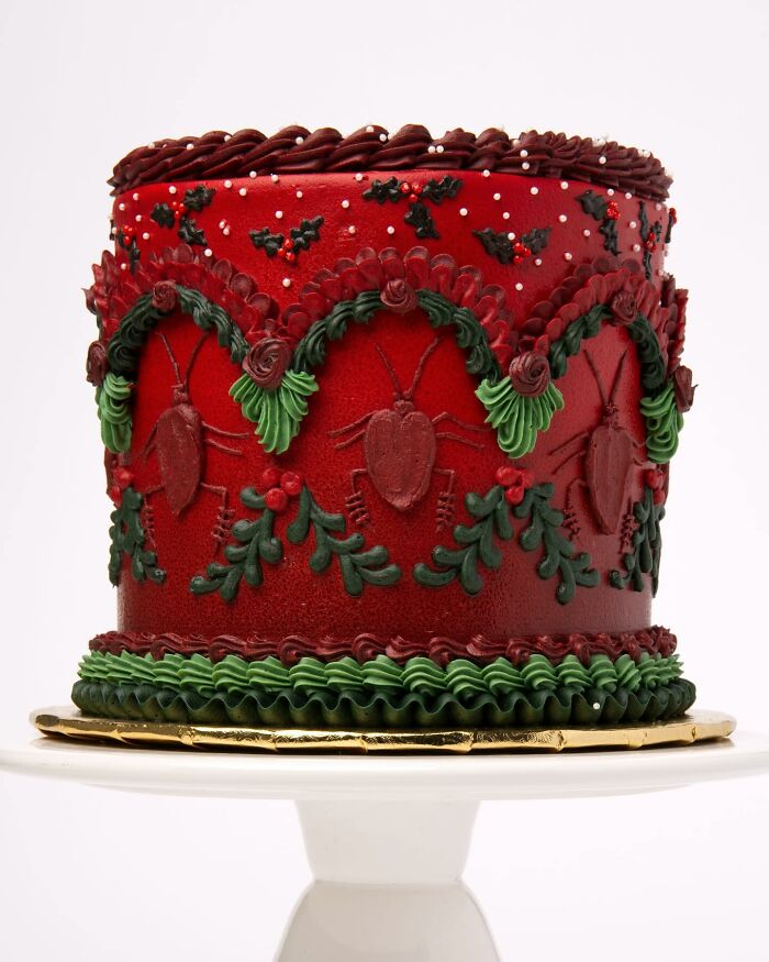 Vegan cake with intricate bug decorations, featuring red and green icing, displayed on a white stand.