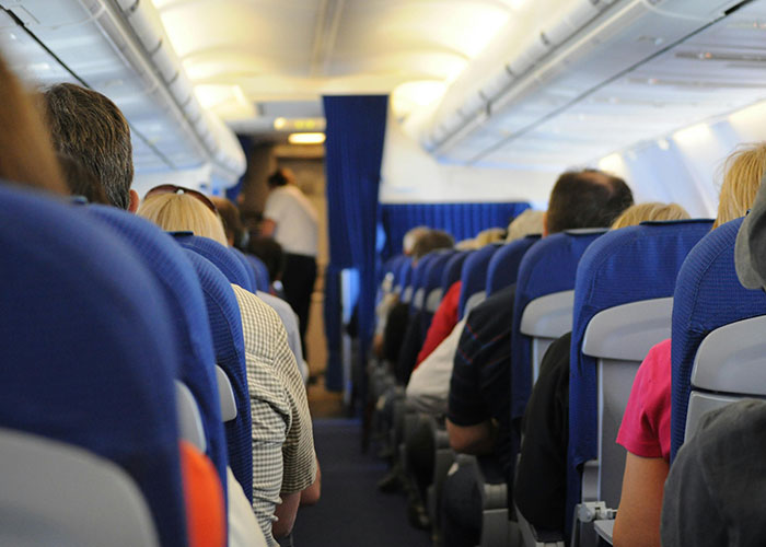 Plane interior with passengers seated, view towards the front and aisle.