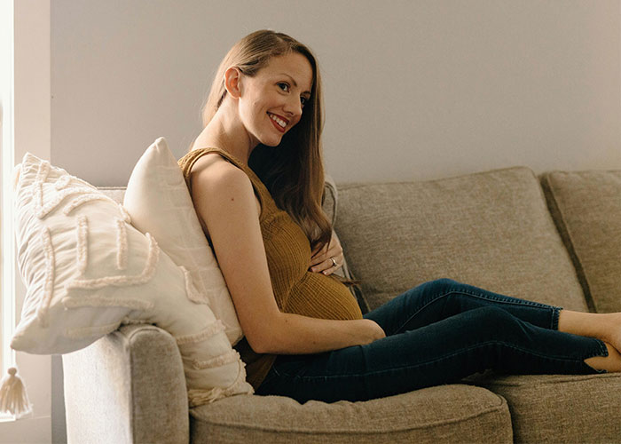 Pregnant woman smiling on a sofa, showcasing unrealistic movie moments with perfect serenity.