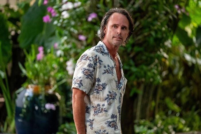 Actor in floral shirt surrounded by lush greenery, embodying personal style essentials.