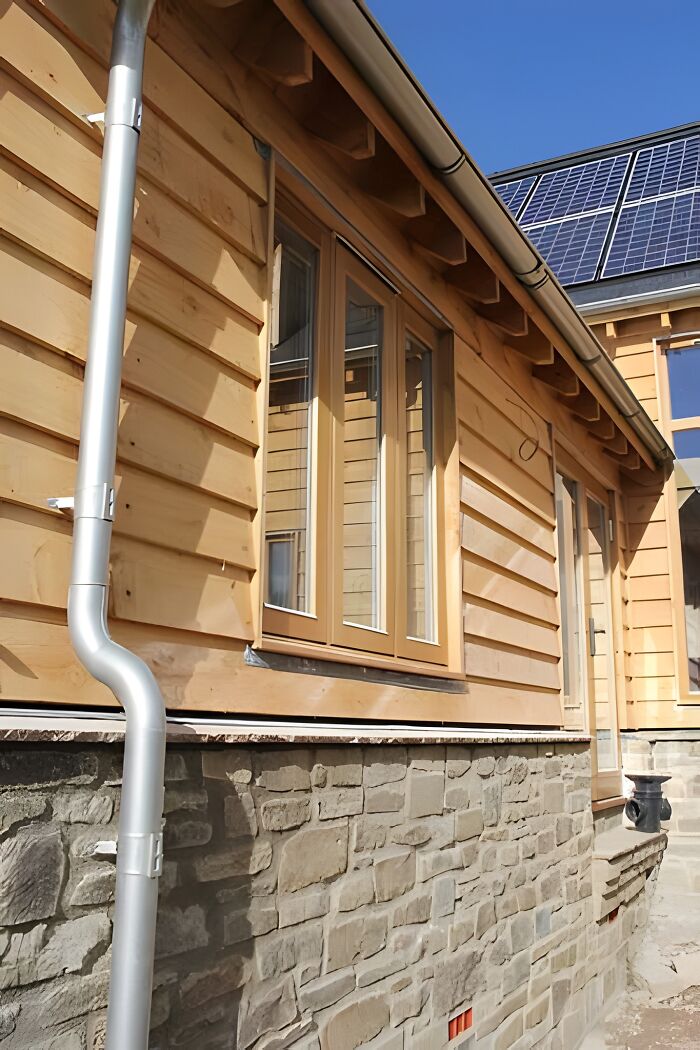 Modern wooden house exterior showcasing woodworking ideas with natural wood siding, windows, and stone foundation under clear sky.