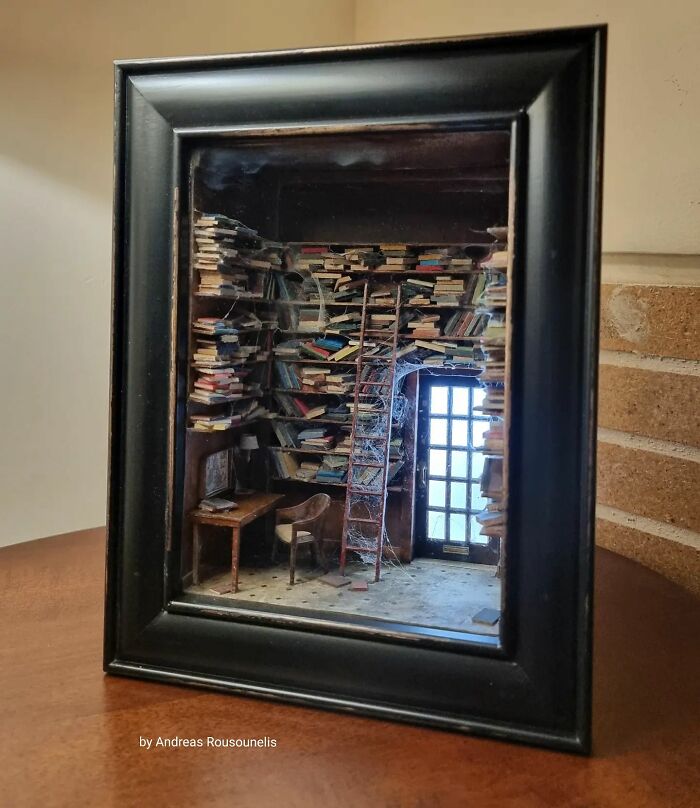 Miniature library scene with stacked books, a ladder, and a desk, framed in black.