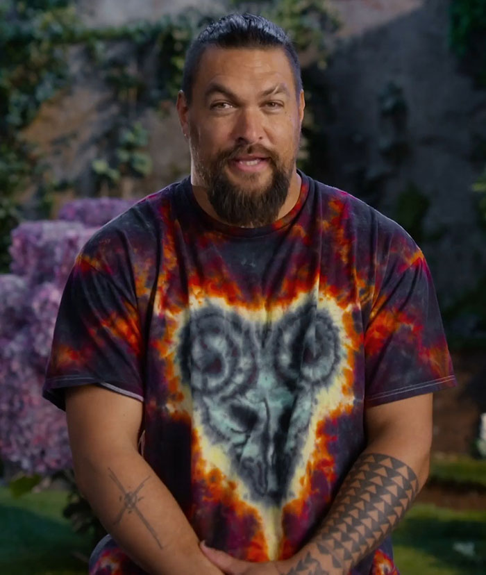 Man in a colorful shirt with tattoos, standing outdoors.
