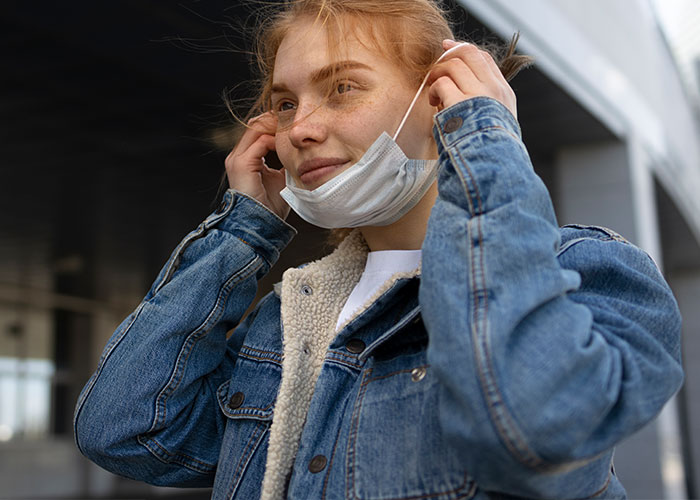 Young woman in a denim jacket adjusting a face mask, illustrating wild rumors turned true.