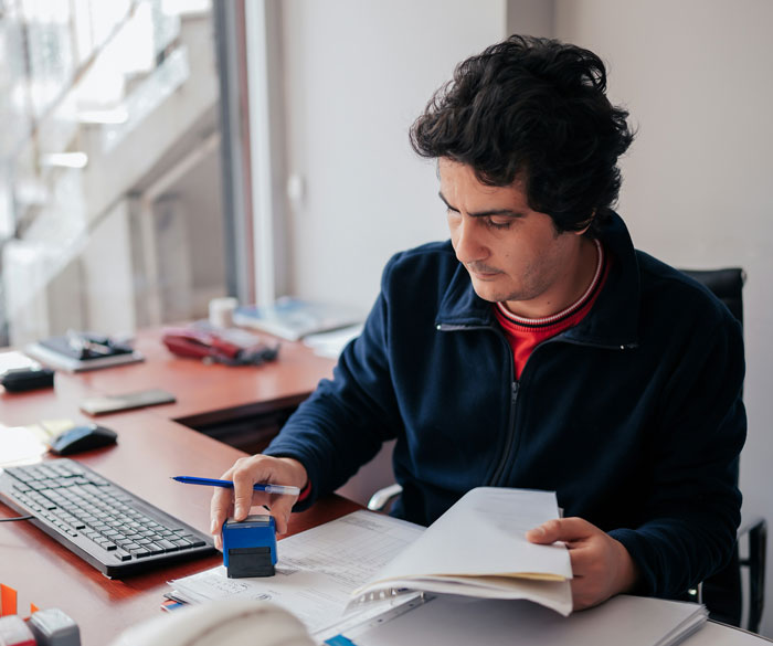 Man stamping papers at desk while reviewing documents, illustrating creative ways to submit SEO deliverables.