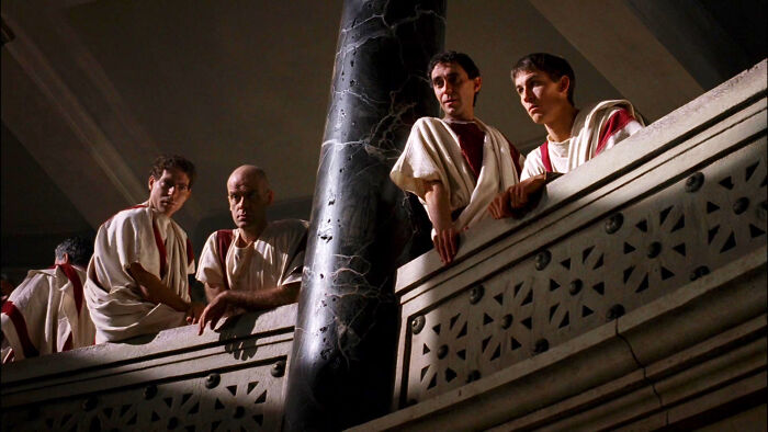 Characters in a historical setting on a balcony, dressed in period costumes, depicting a visually engaging scene from a TV show.