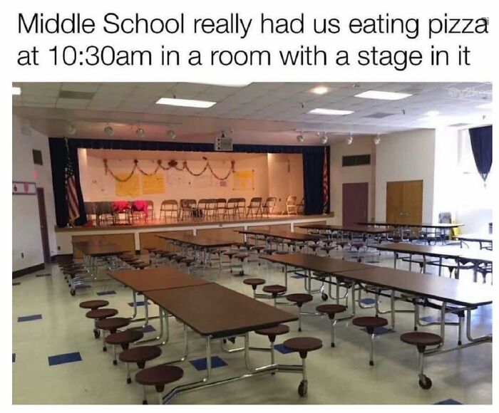Empty middle school cafeteria with pizza tables and chairs in a room with a stage, reflecting funny memes about school lunch times.