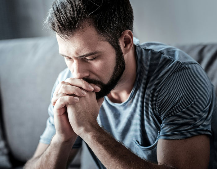 Man looking stressed while sitting on a couch after boss canceled doctor's appointment.