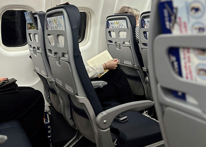 Passenger on a plane reading a book, with a phone on the seat, illustrating unusual plane behavior.