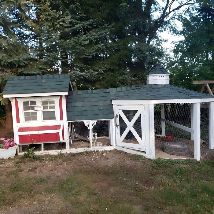 Wooden chicken coop with green roof and white trim surrounded by trees, showcasing creative woodworking ideas outdoors.