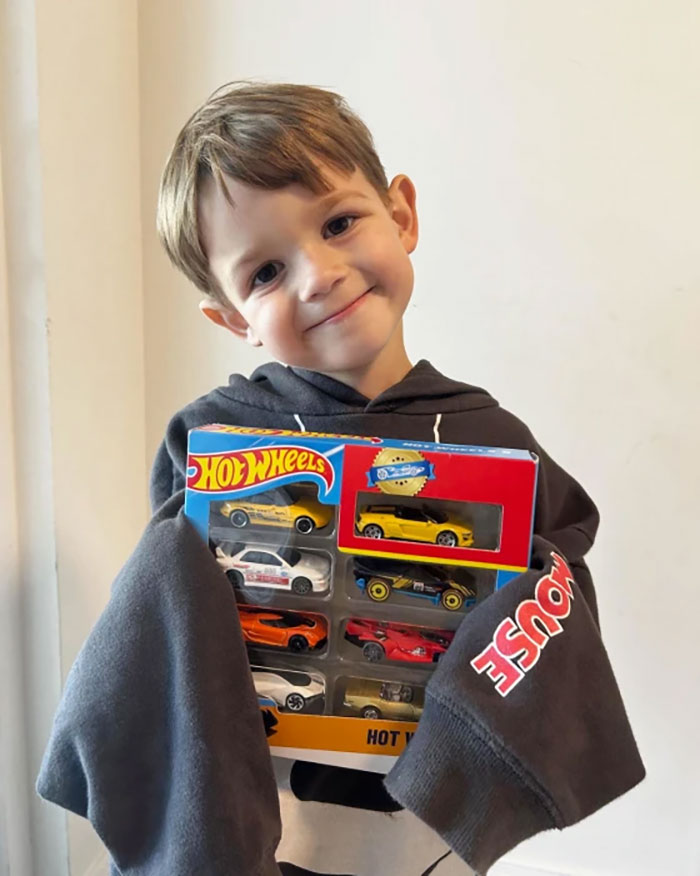 Child smiling with Hot Wheels cars, celebrating birthday surprise from local sports car lovers.