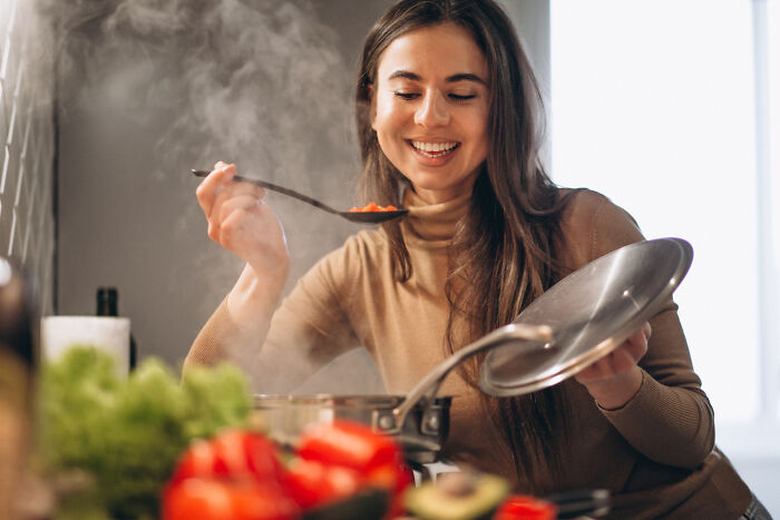 A woman enjoying affordable treats while cooking, with colorful ingredients and steam rising from a pot.