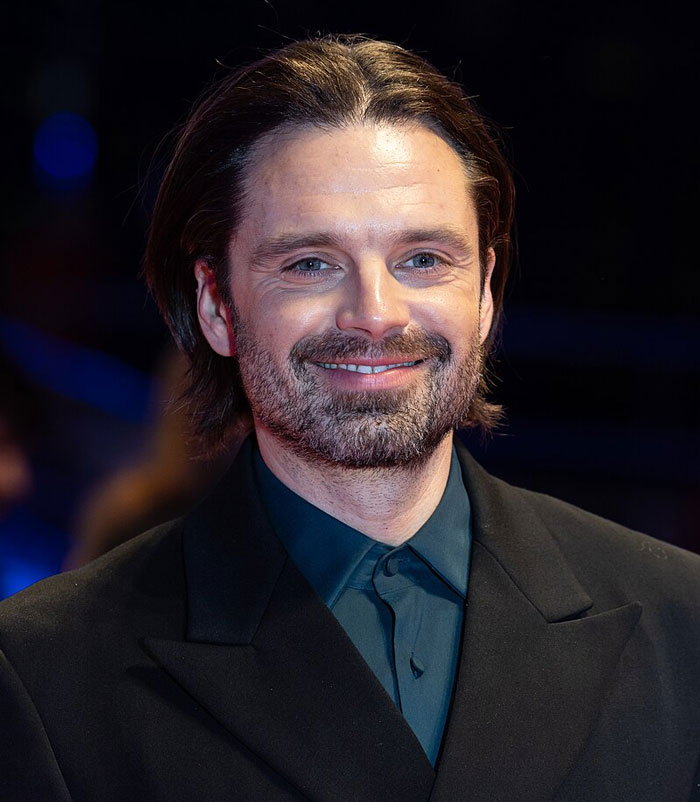 Smiling bearded man in a dark suit on a red carpet at an event, showcasing beloved star in a wholesome setting.