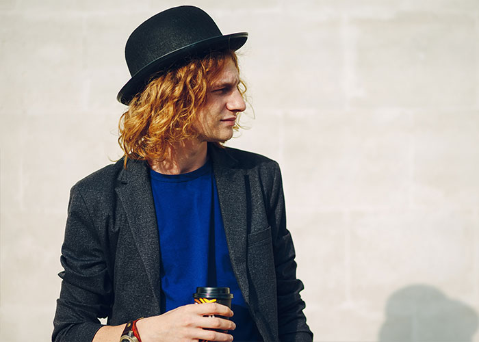 Man in black hat and blazer holding a coffee, illustrating Duke Dennis aesthetic outdoors.