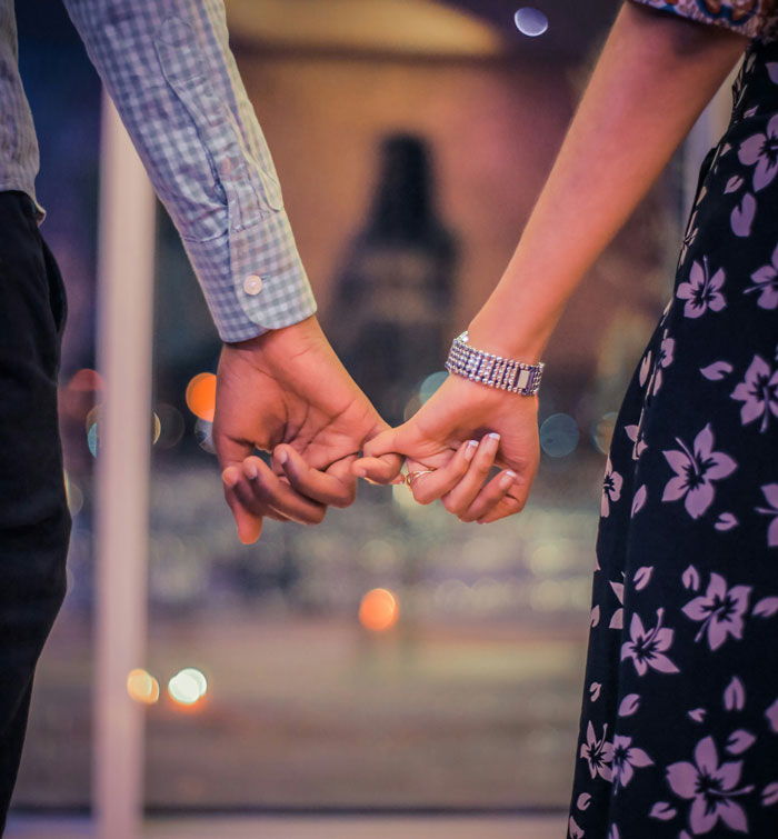 Close people holding hands in an intimate setting, with focus on their fingers intertwined gently.